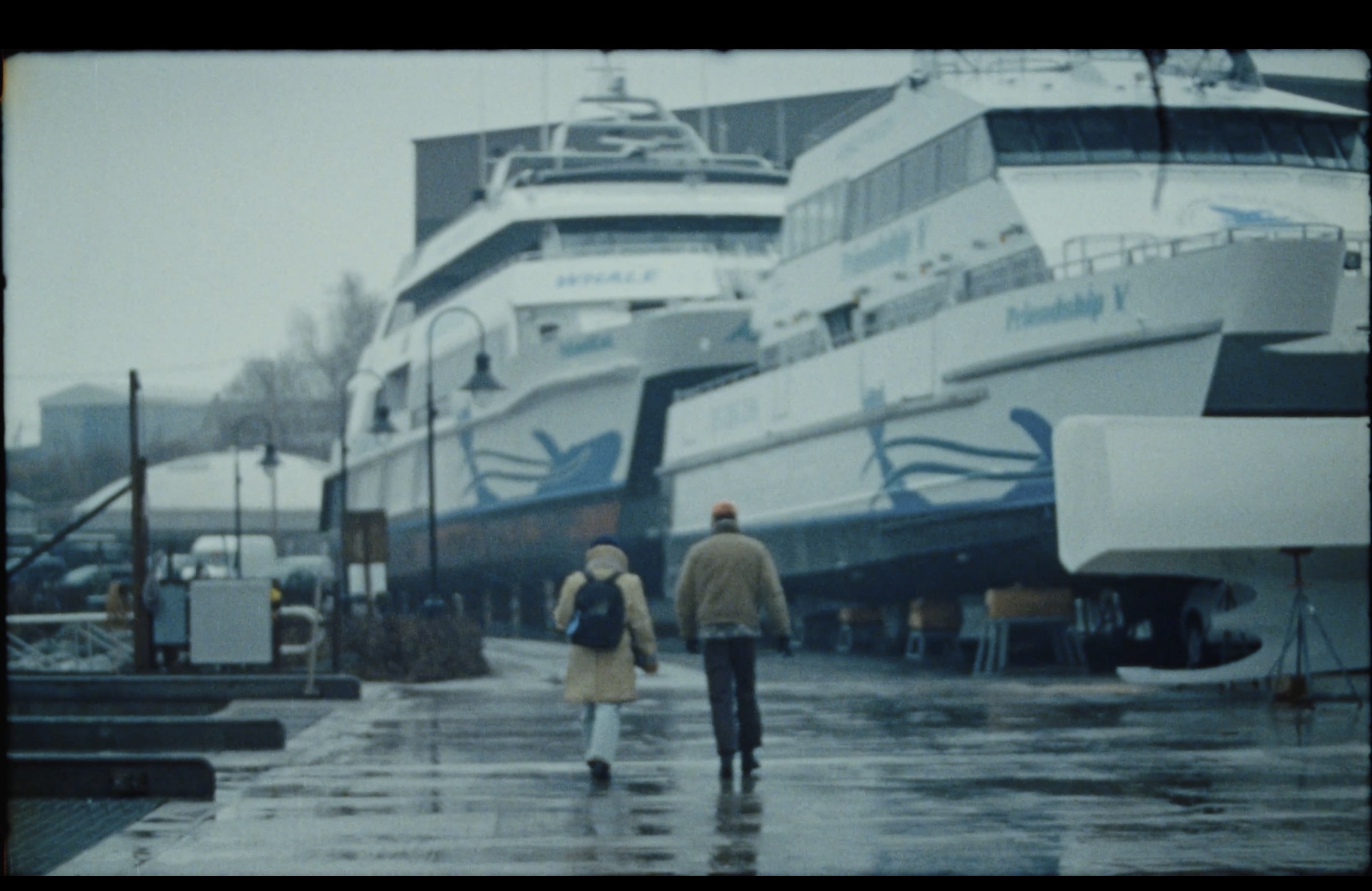 Two figures walking near a ferry in rain