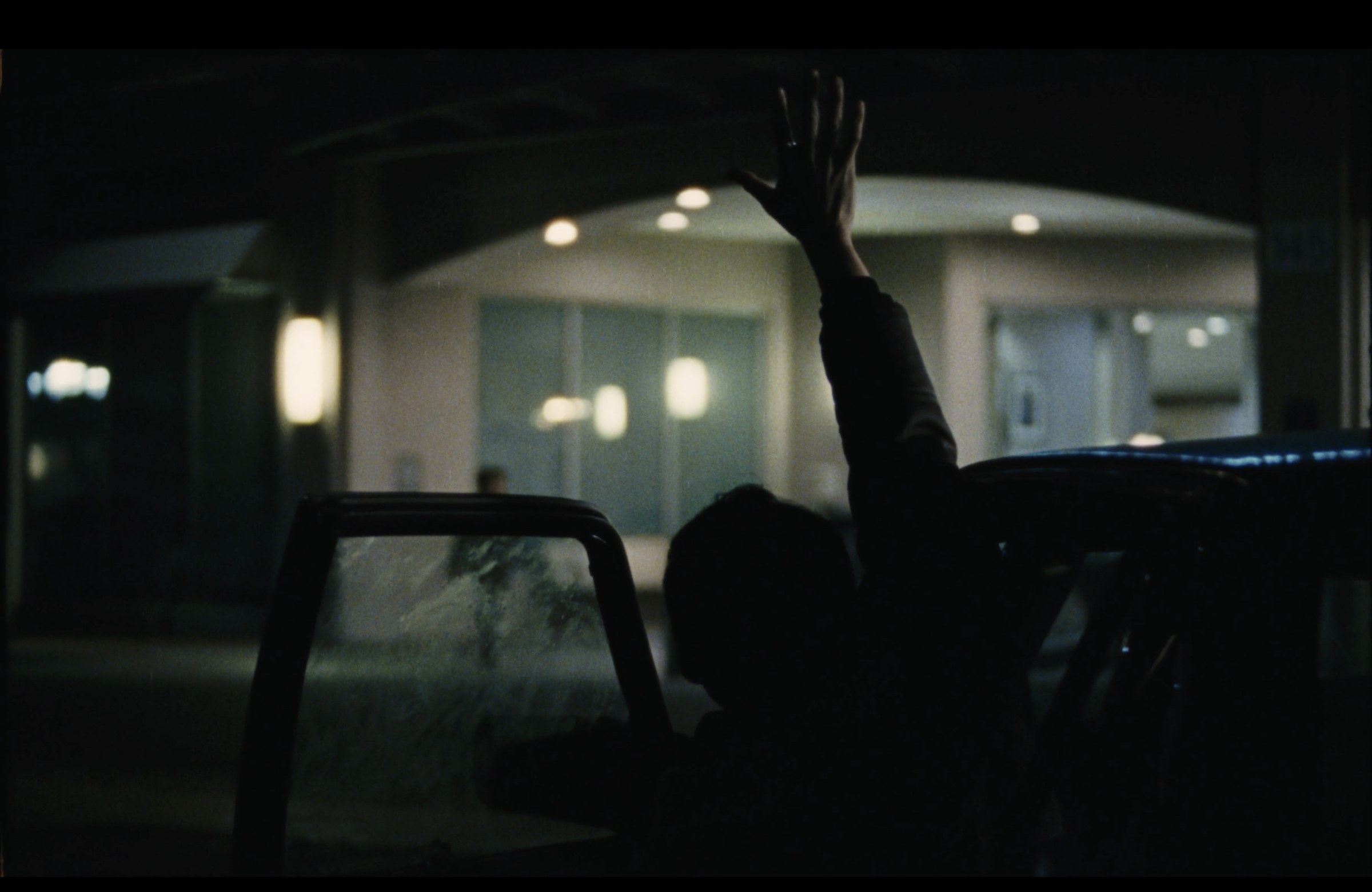 Night exterior with a figure beside a car